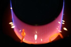 Auf der runden Oberfläche eines Brenners ist eine Flammenbildung in den Farben von Orange über Rot bis Blau zu sehen. 