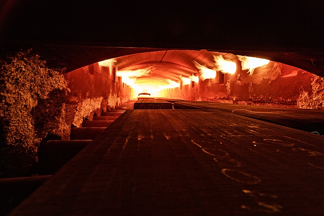 Through a long tunnel, which shimmers reddish due to fire on the left and right walls, .large metal plates move over metallic rollers.