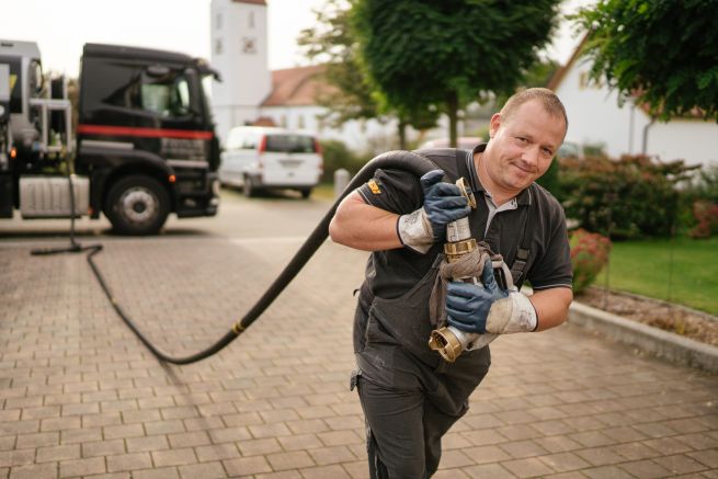 Betankung mit paraffinischem Heizöl_Foto: en2x_web Ein Mann zieht einen langen Schlauch mit Heizöl-Füllstutzen vom Tankwagen.